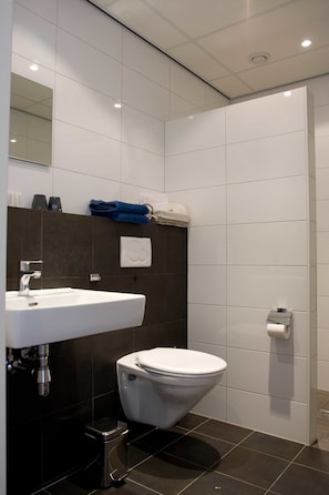 A modern bathroom with a white sink, dark tiles, a toilet, and a towel rack. - B&B Erve Fakkert (Rossum)
