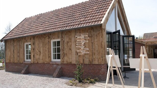 A wooden building with a sloped roof and a glass door. There are wooden easels outside. - B&B Erve Fakkert (Rossum)