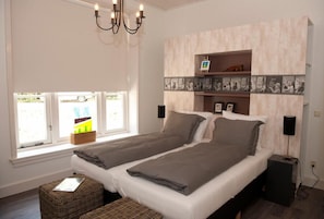 A bedroom with two beds, a large window, a chandelier, and a wall-mounted shelf with pictures. - B&B Erve Fakkert (Rossum)