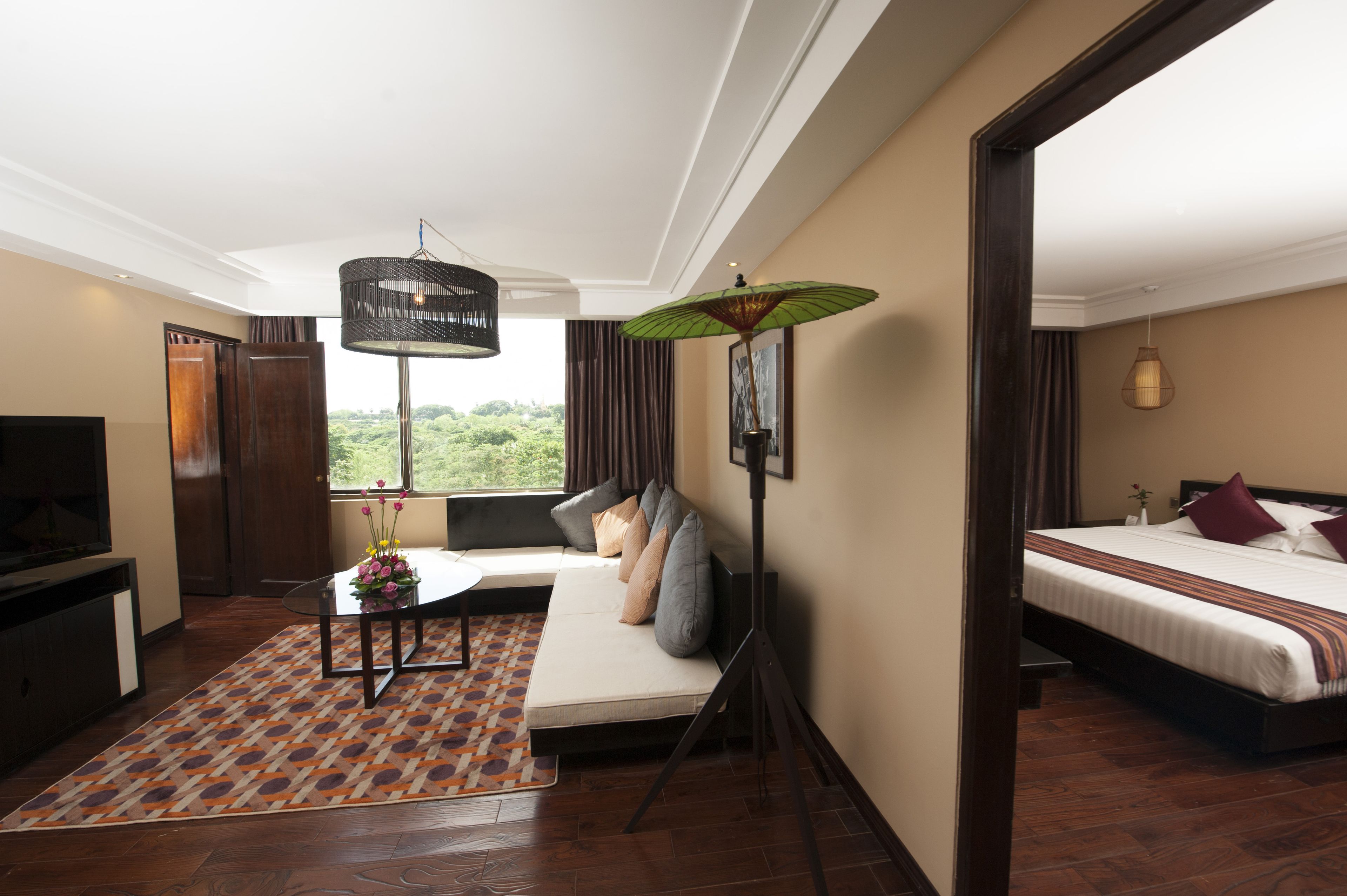 Habitación de hotel moderna con sofá, cama, televisor y un amplio ventanal con vista a la vegetación.