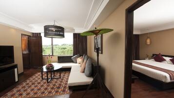 Habitación de hotel moderna con sofá, cama, televisor y un amplio ventanal con vista a la vegetación.
