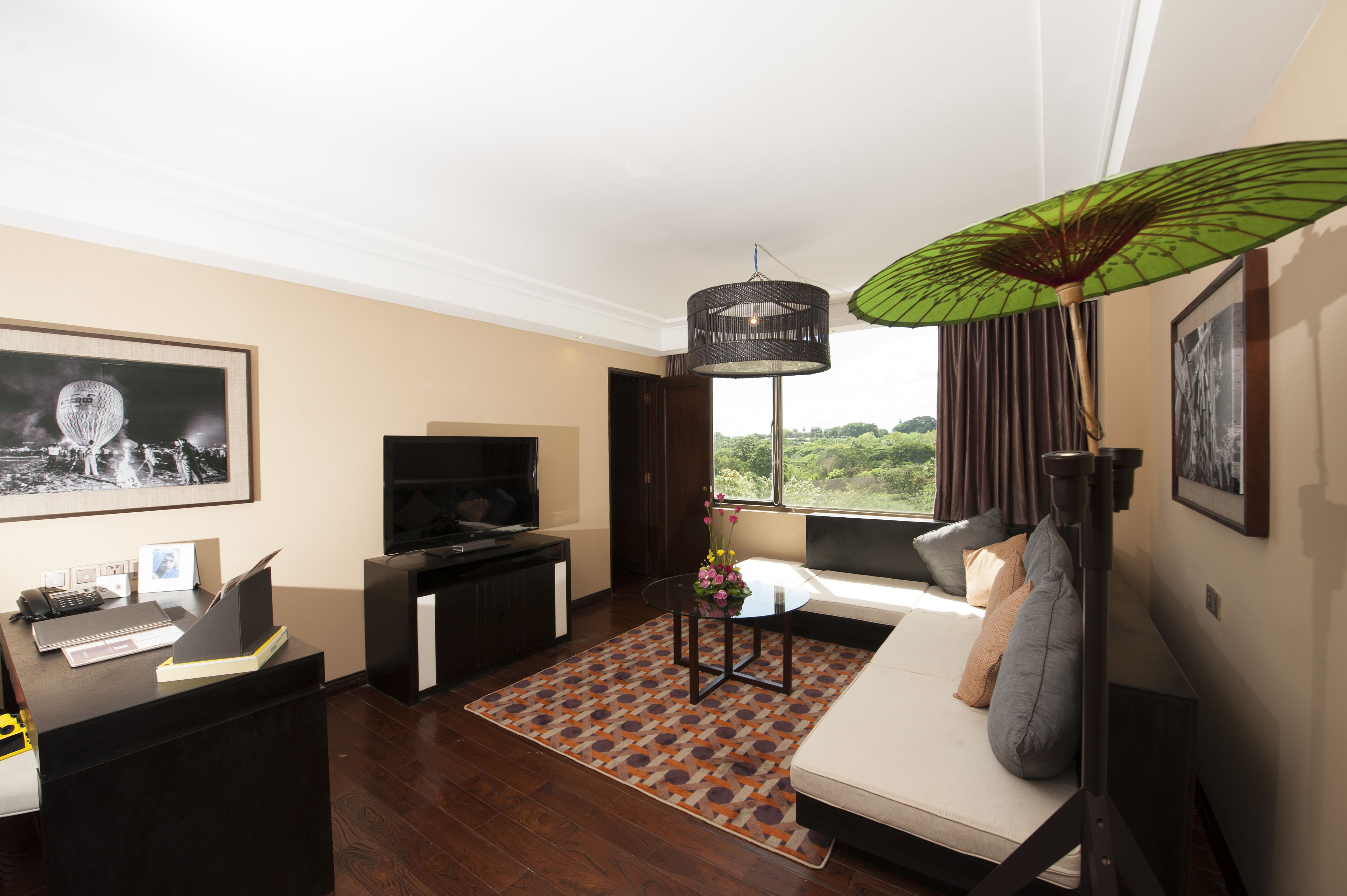 A modern hotel room with a sofa, TV, desk, and a view of greenery.