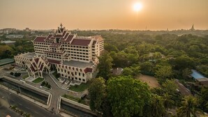 Un edificio grande de varios pisos con un estilo arquitectónico tradicional, rodeado de abundante vegetación y un cielo despejado.