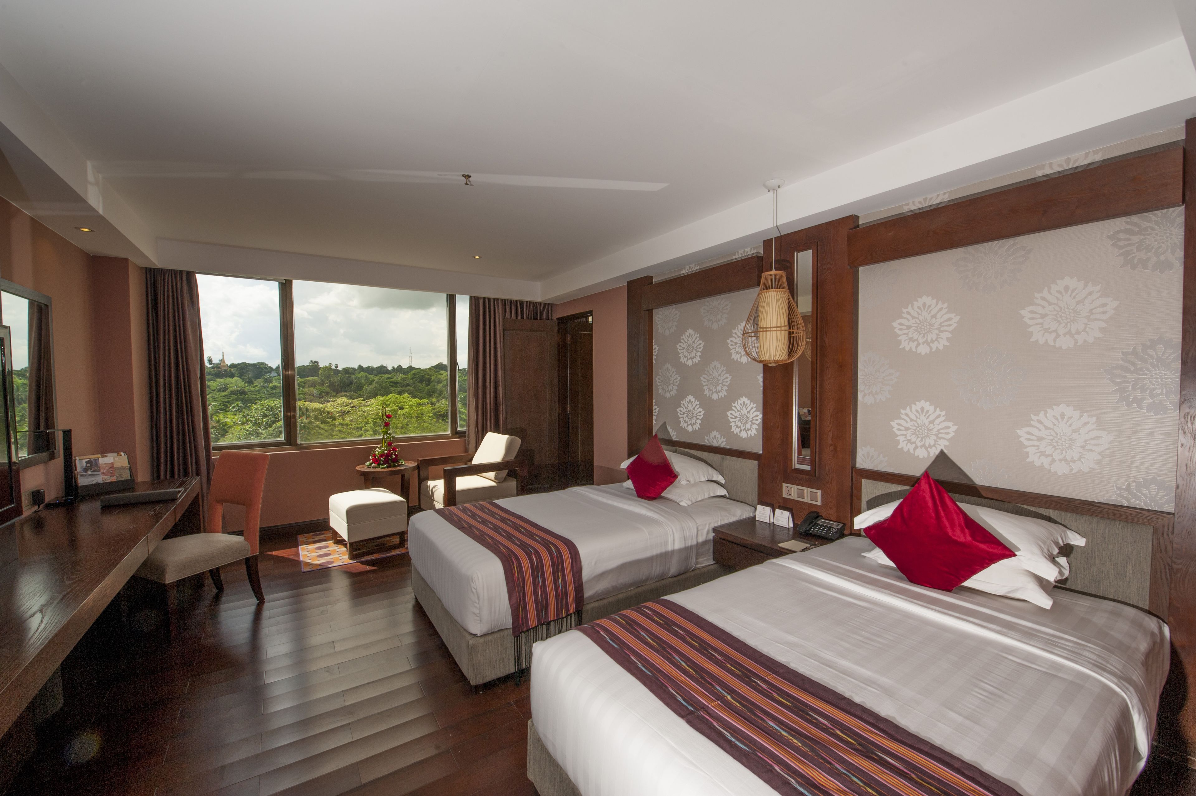 A hotel room with two beds, a desk, a chair, and a view of greenery.