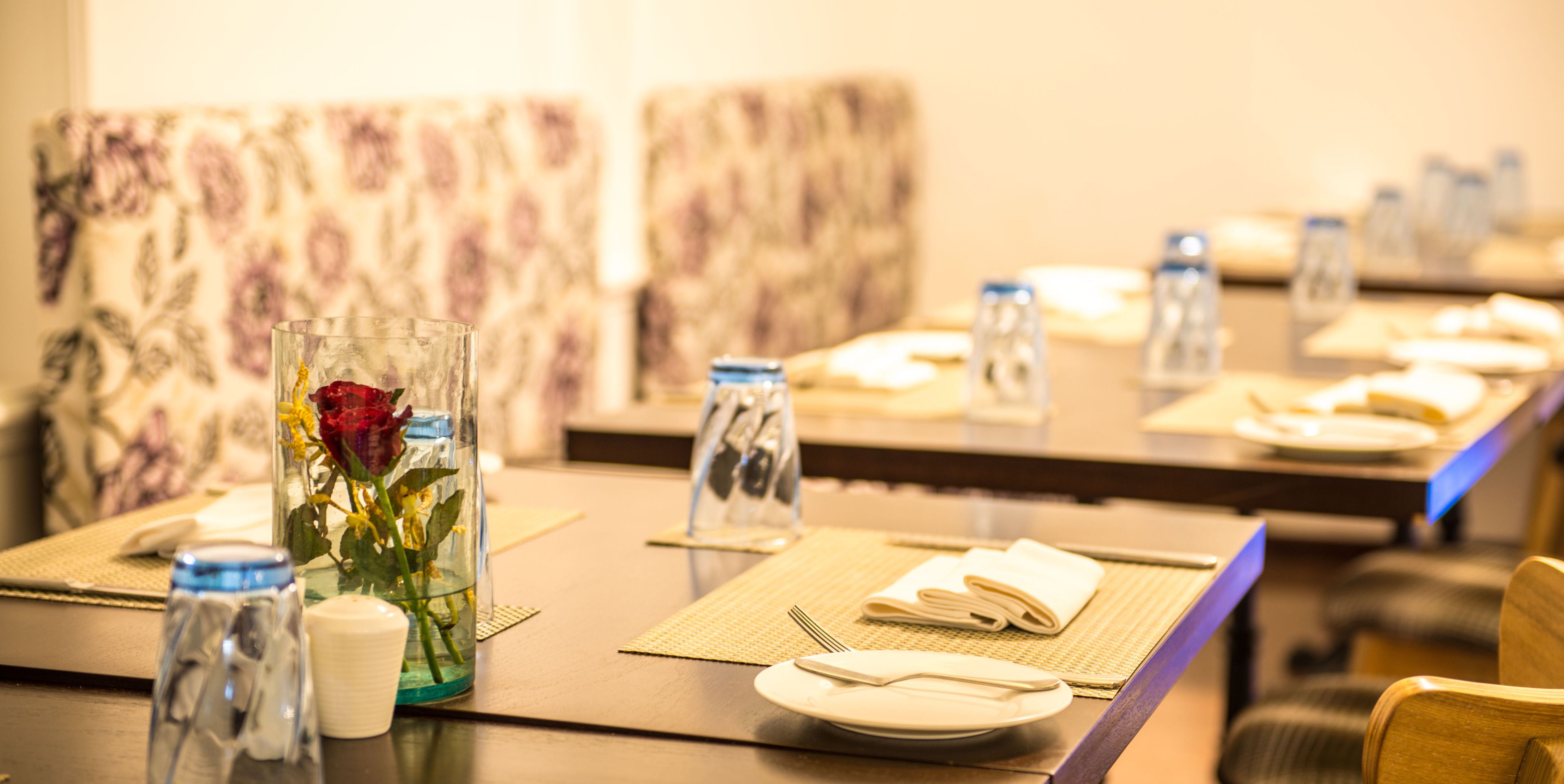 Una mesa de comedor dispuesta con platos, cubiertos y un florero con una flor.