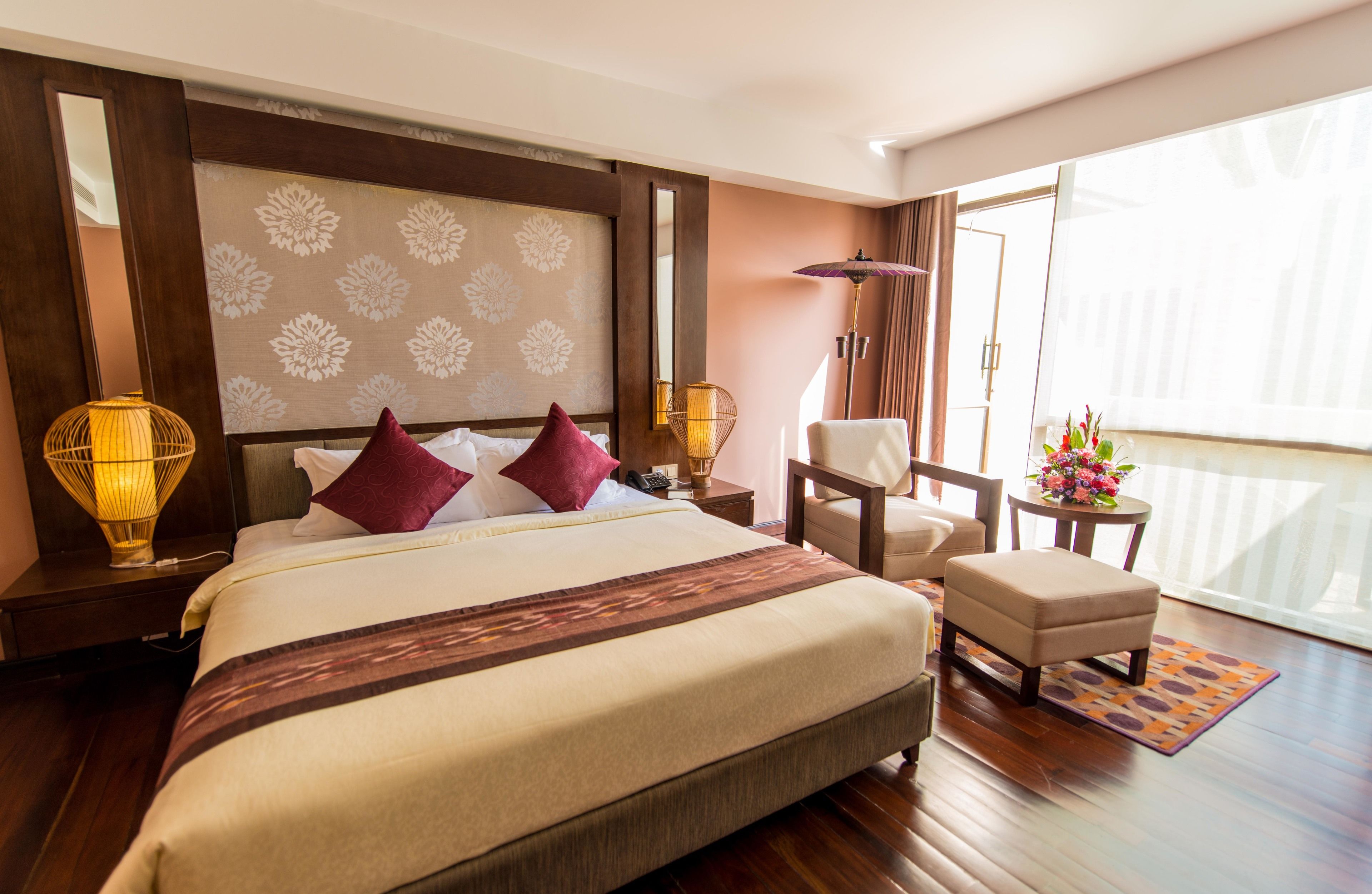 Habitación de hotel con una cama grande, una silla, una mesita con flores y vistas al exterior.