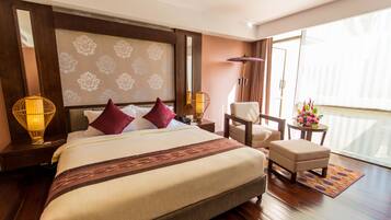 Habitación de hotel con una cama grande, una silla, una mesita con flores y vistas al exterior.