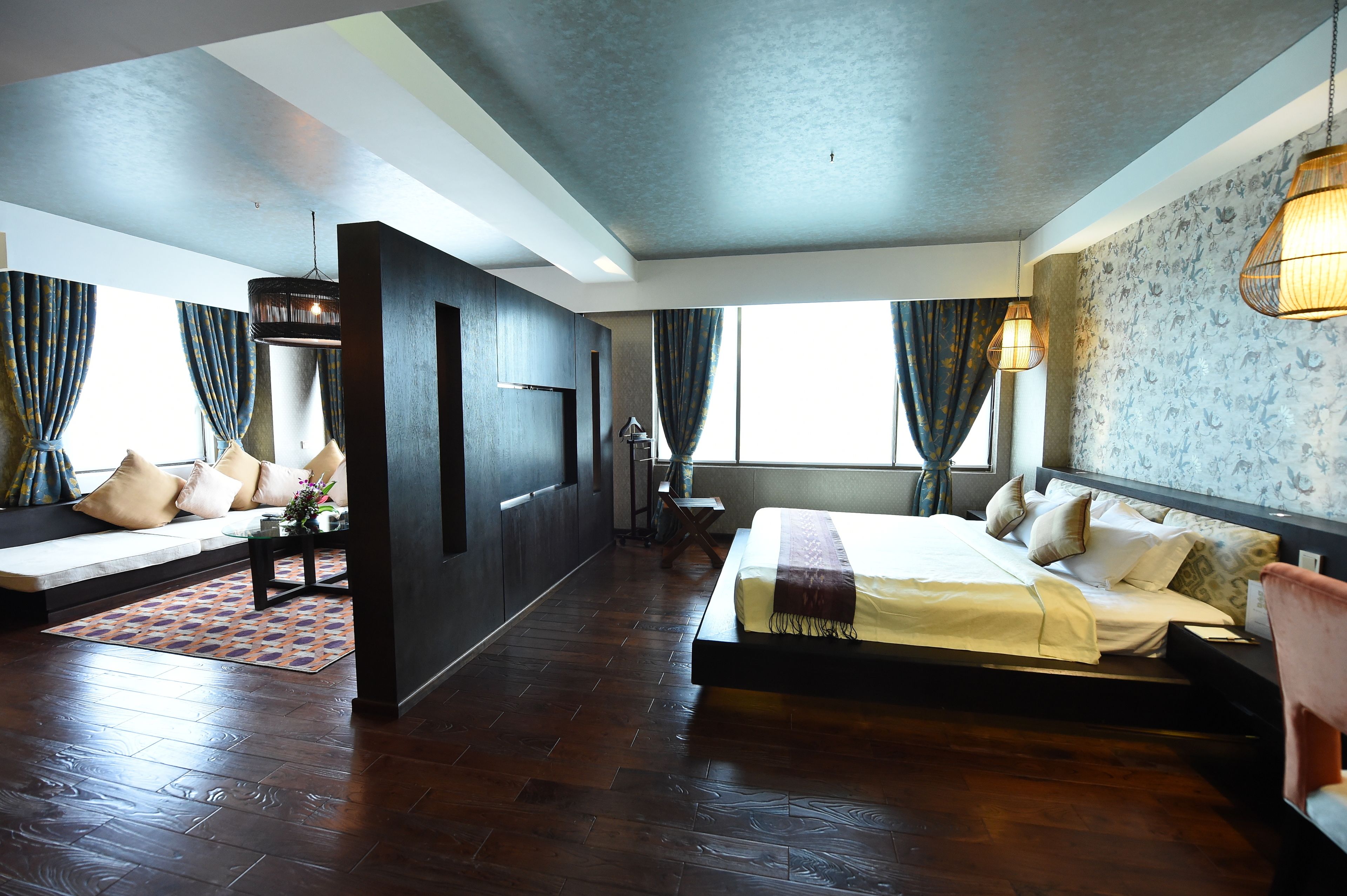 A modern hotel room with a large bed, a seating area with a sofa and armchairs, a small table, and a view of the outdoors.
