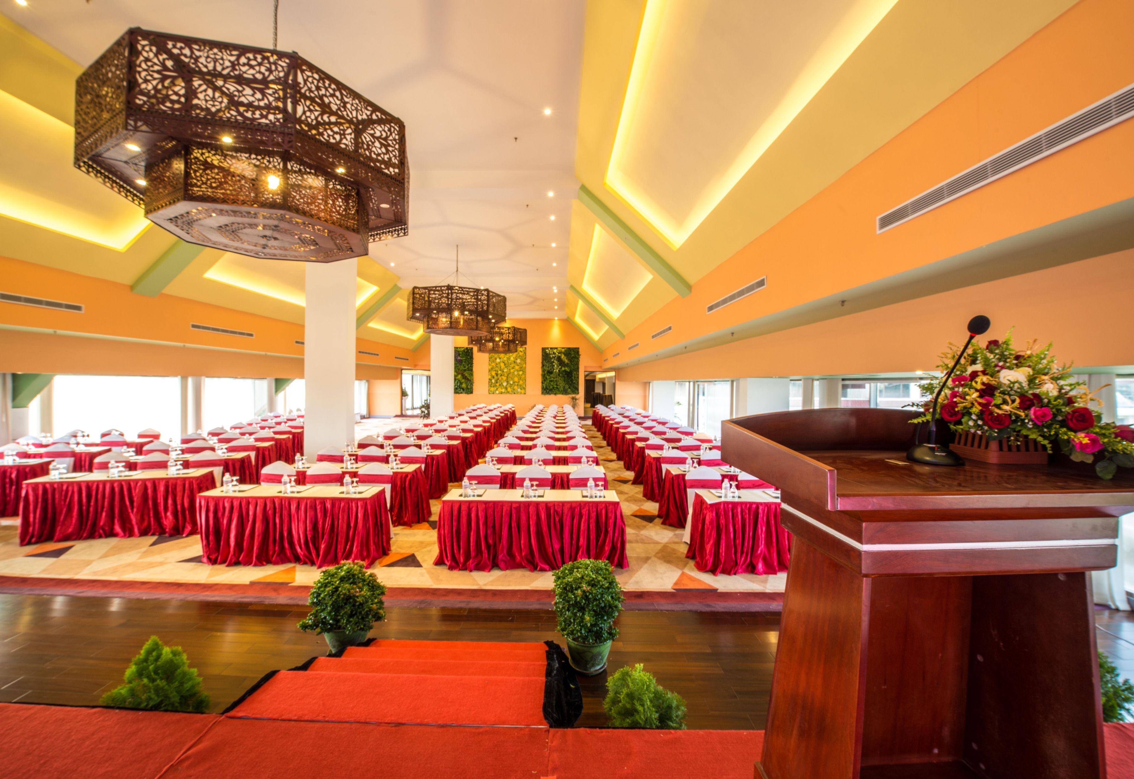 A large conference room with rows of tables, a podium, and decorative lighting.