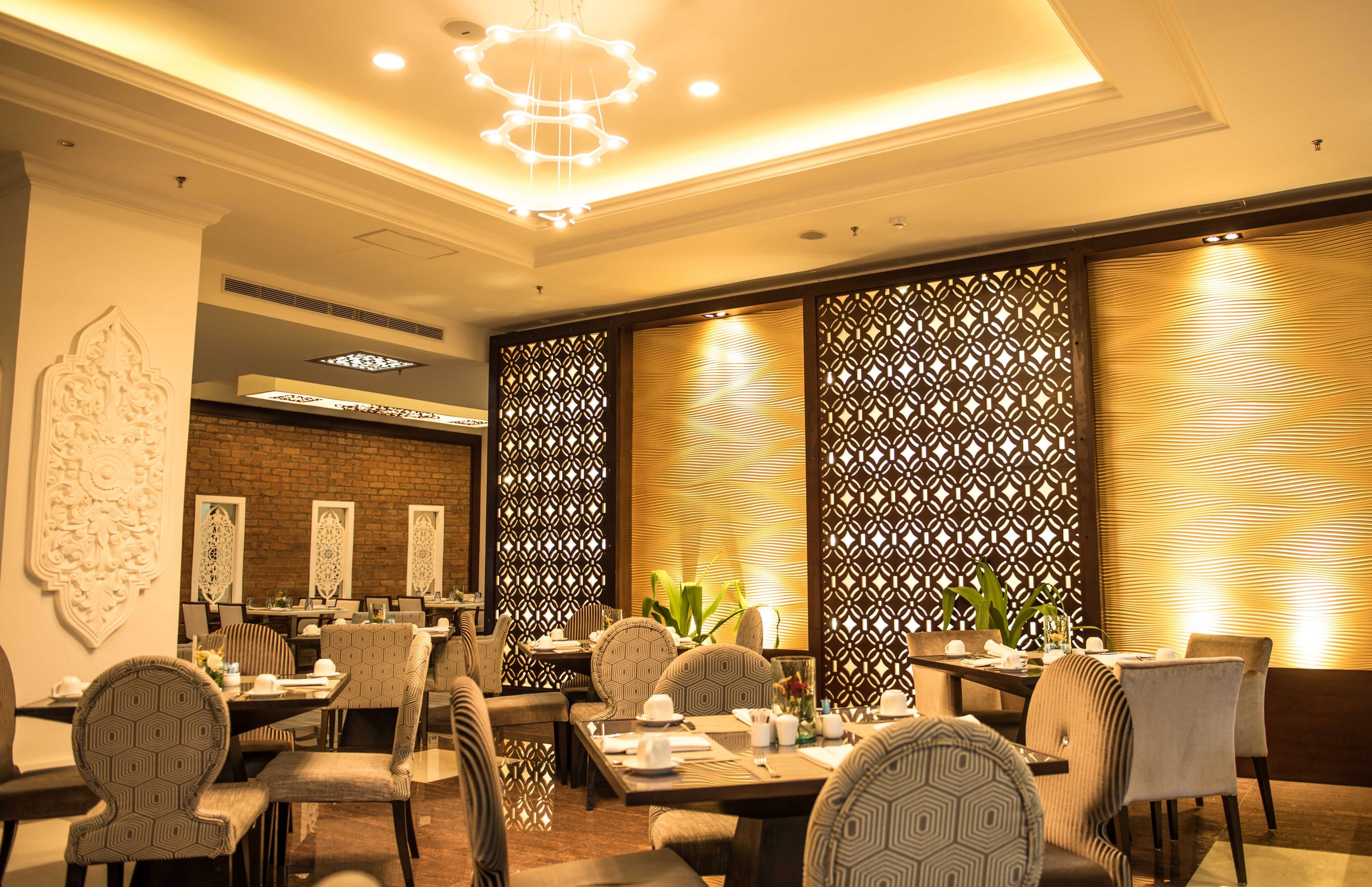 A dining area with multiple tables and chairs, decorative wall panels, and a chandelier.