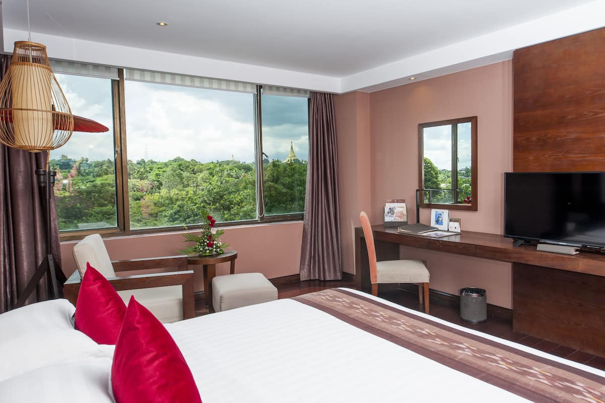Ein Hotelzimmer mit einem großen Bett, einem Schreibtisch mit Computer, einem Fernseher und Blick ins Grüne.