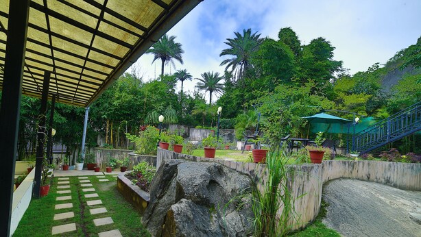 A covered outdoor area with a stone pathway, potted plants, and a staircase leading to a higher level. - Hotel Shiv Villa by SAH (Abu Road)