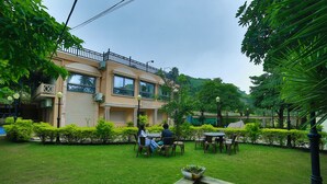 A courtyard with a two-story building, outdoor seating, and a small water feature. - Hotel Shiv Villa by SAH (Abu Road)