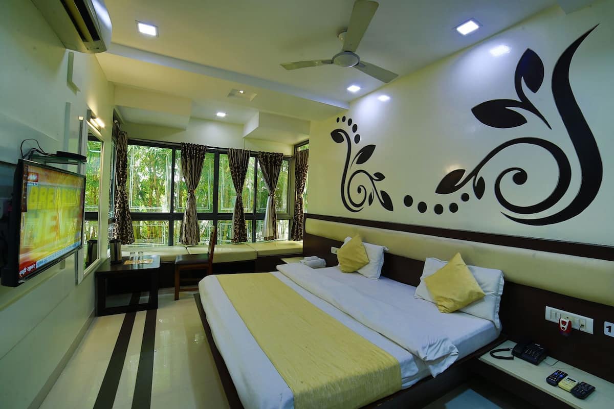 A hotel room with a bed, bedside table, TV, window with curtains, and a decorative wall design.
