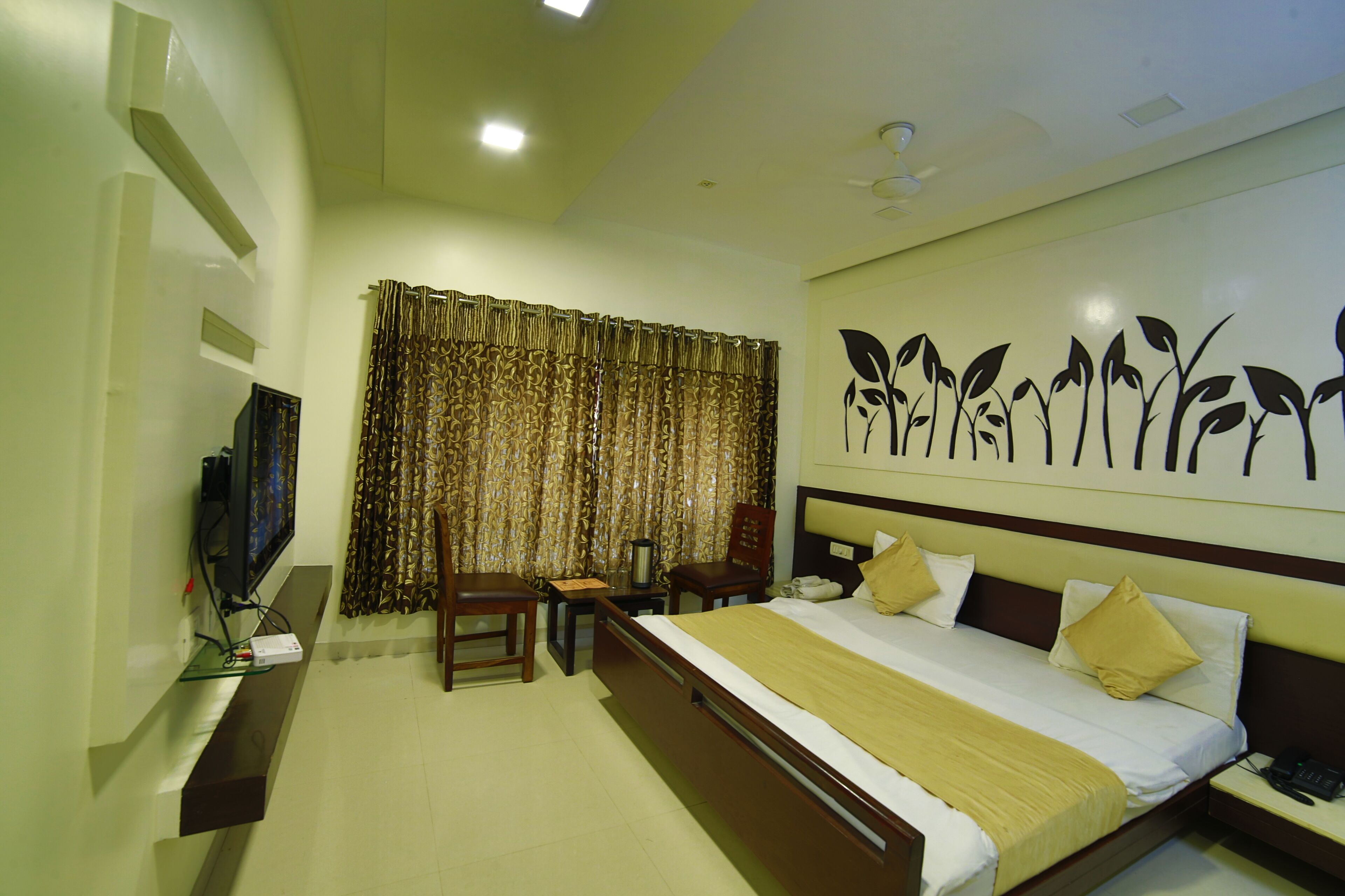 A hotel room with a bed, bedside table, TV, and curtains.