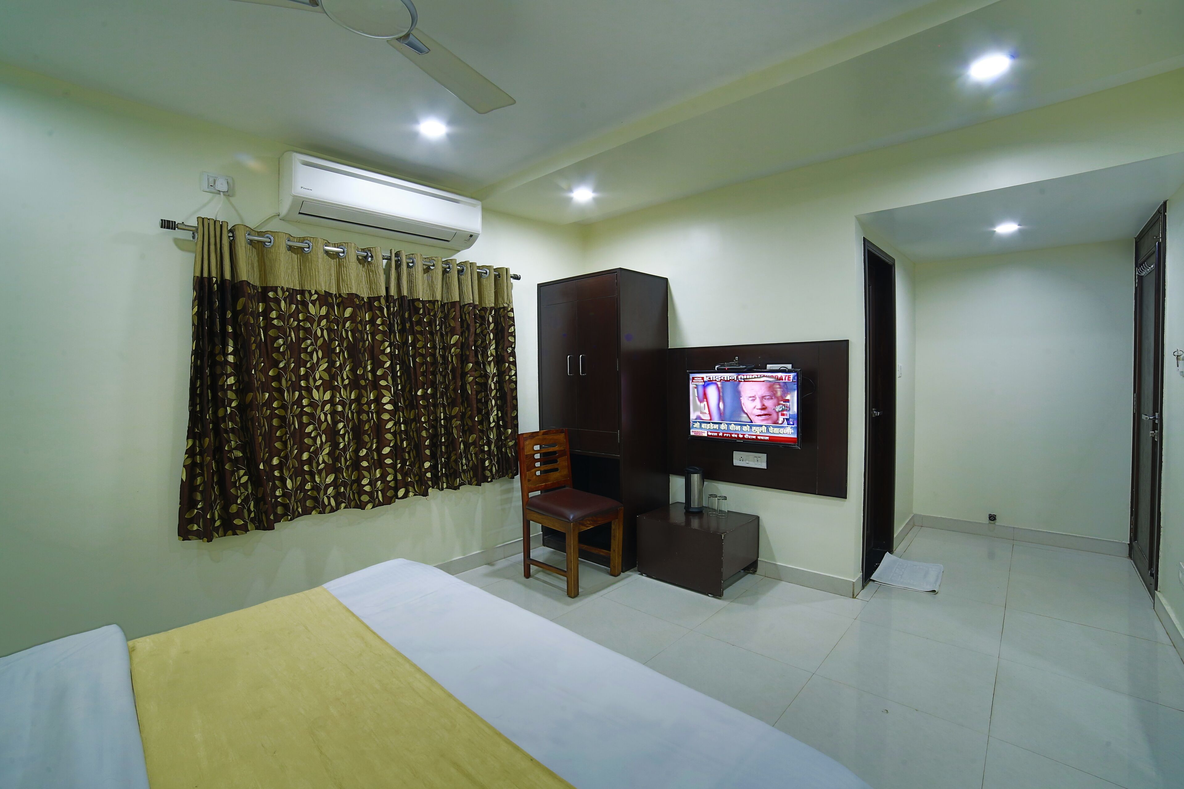A hotel room with a bed, a chair, a TV, an air conditioner, and a wardrobe.