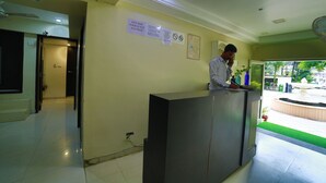 A reception area with a receptionist, a reception desk, and a wall with informational signs. - Hotel Shiv Villa by SAH (Abu Road)