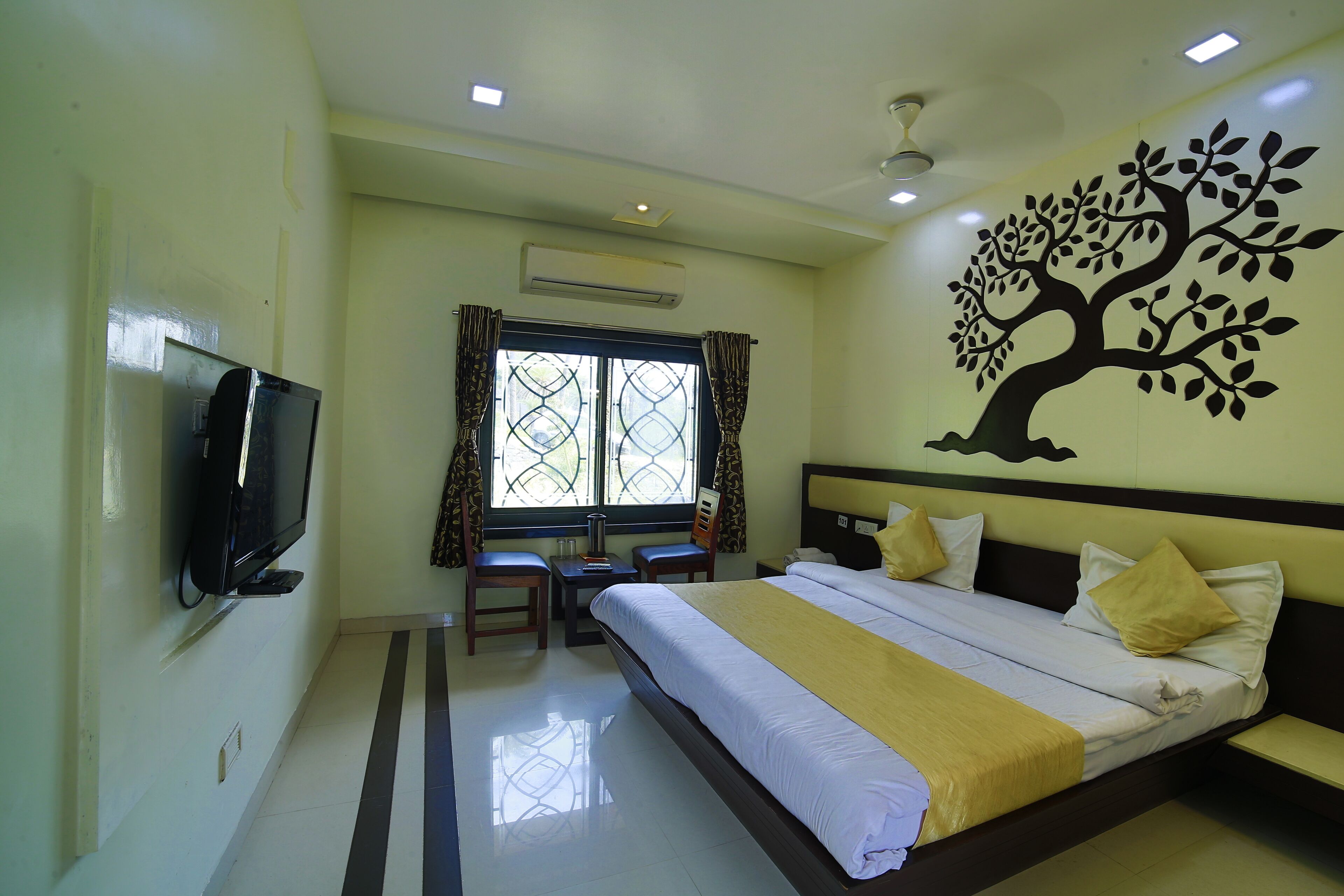A hotel room with a bed, a TV, a desk, and a window with curtains.