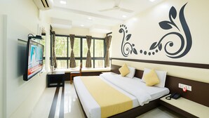 A hotel room with a bed, a TV mounted on the wall, a desk, and a window with curtains. - Hotel Shiv Villa by SAH (Abu Road)
