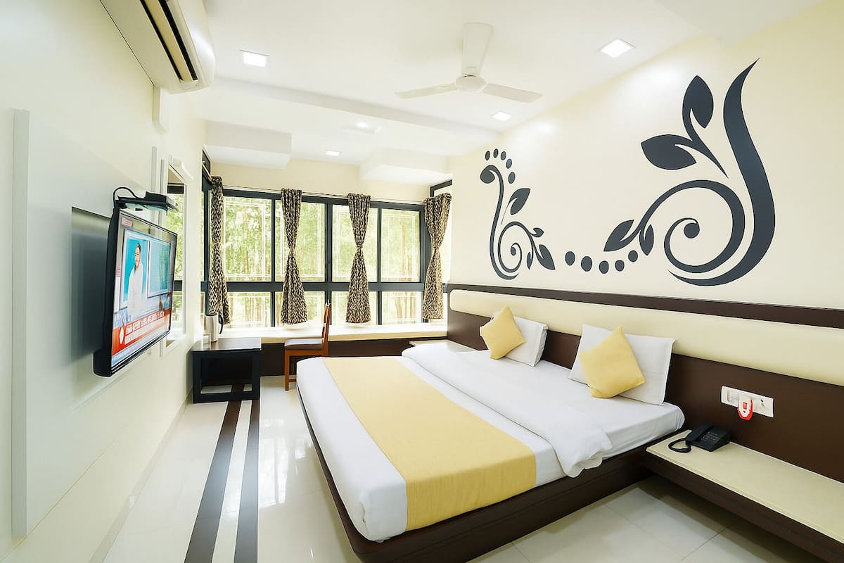 A hotel room with a bed, a TV mounted on the wall, a desk, and a window with curtains.