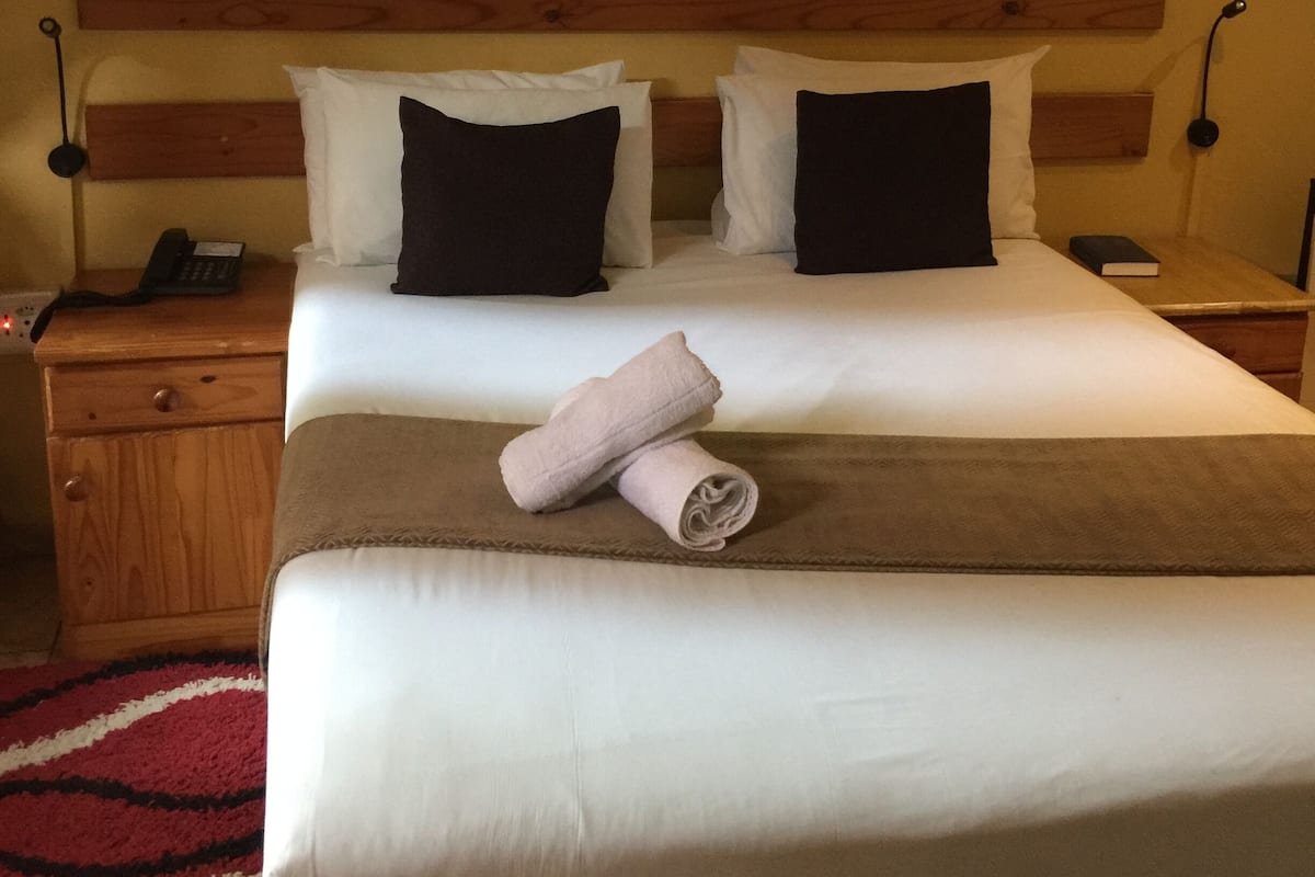 A hotel room with a large bed, two bedside tables, a wooden headboard, and a wall-mounted artwork.