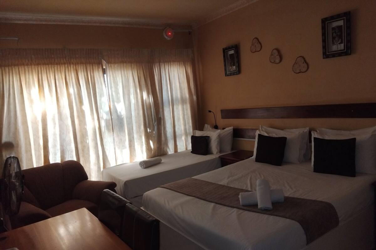 A hotel room with two beds, a wooden table, a chair, and a window with curtains.
