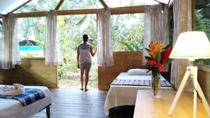 A room with a bed, a small table with a lamp, and a window with curtains. - Lirio Lodge (Pacuarito)