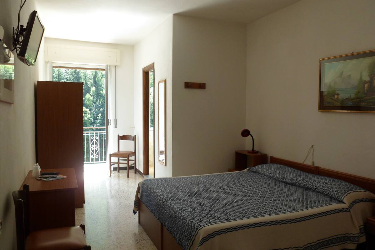 A bedroom with a bed, a desk, a chair, a wardrobe, and a painting on the wall.