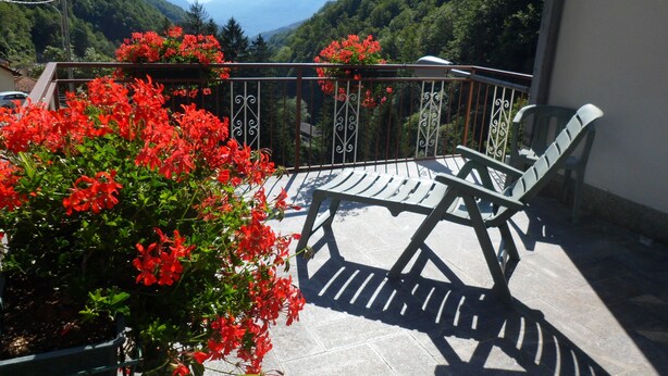 A balcony with a table and chairs, surrounded by red flowers and a view of a mountainous landscape. - Albergo Regina (Bognanco)
