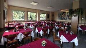 A dining area with tables set for multiple people, large windows, and a painting on the wall. - Albergo Regina (Bognanco)