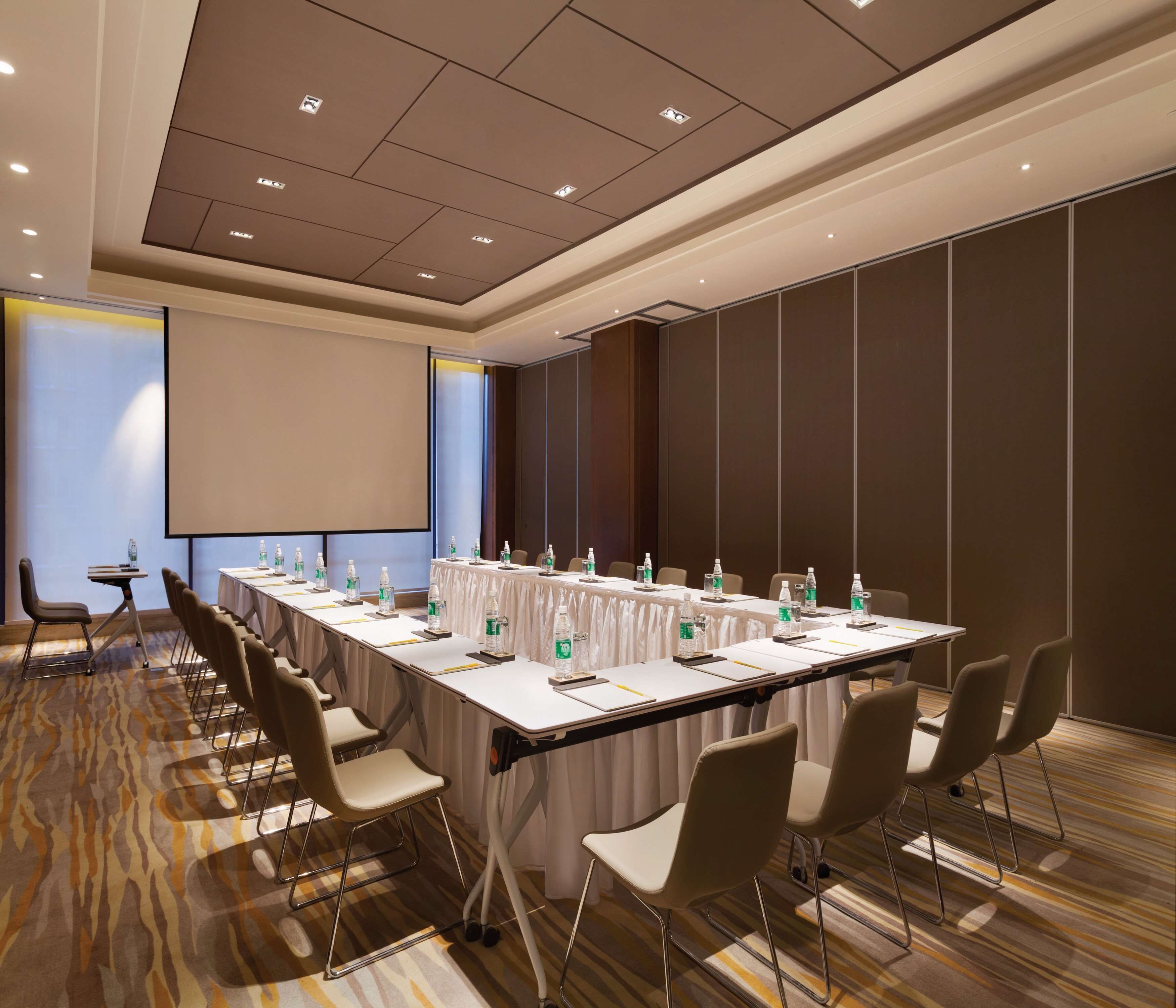 A conference room with a long table, chairs, a projector screen, and water bottles.