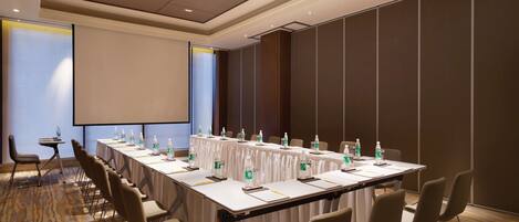 A conference room with a long table, chairs, a projector screen, and water bottles.