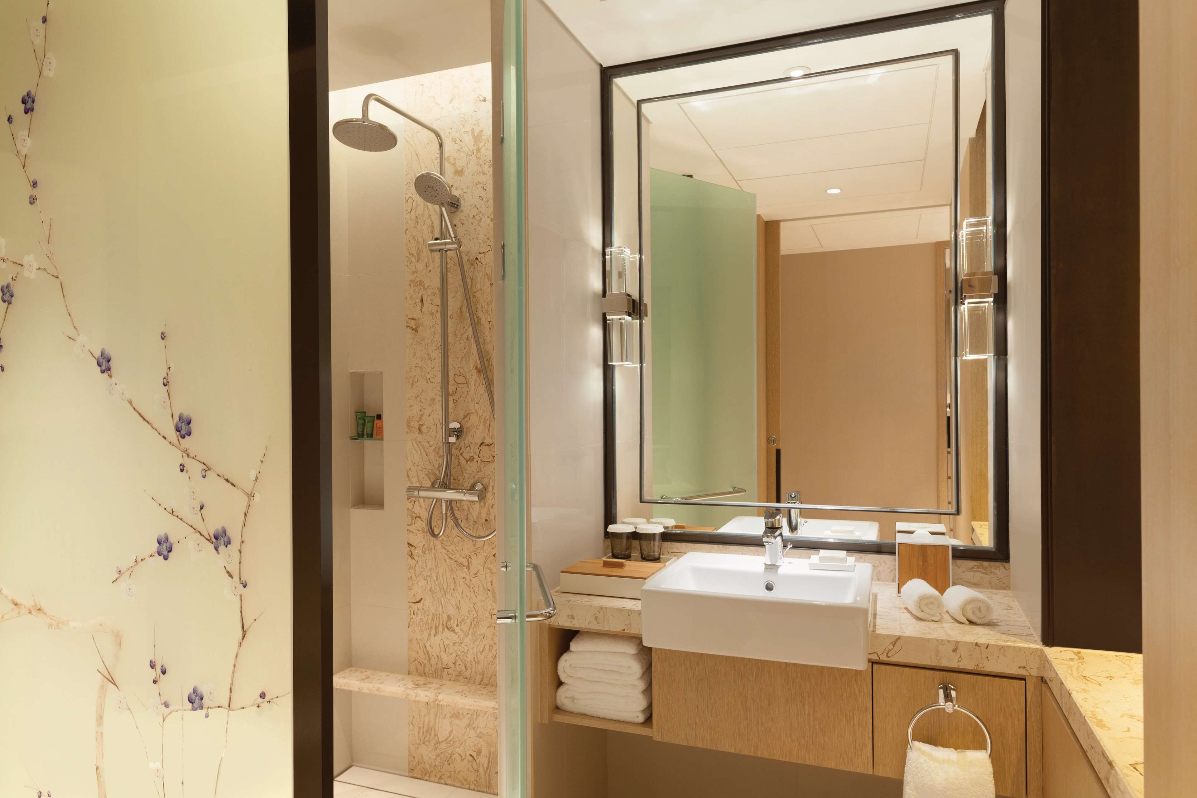 Un baño moderno con cabina de ducha de vidrio, un espejo grande y encimera de mármol.