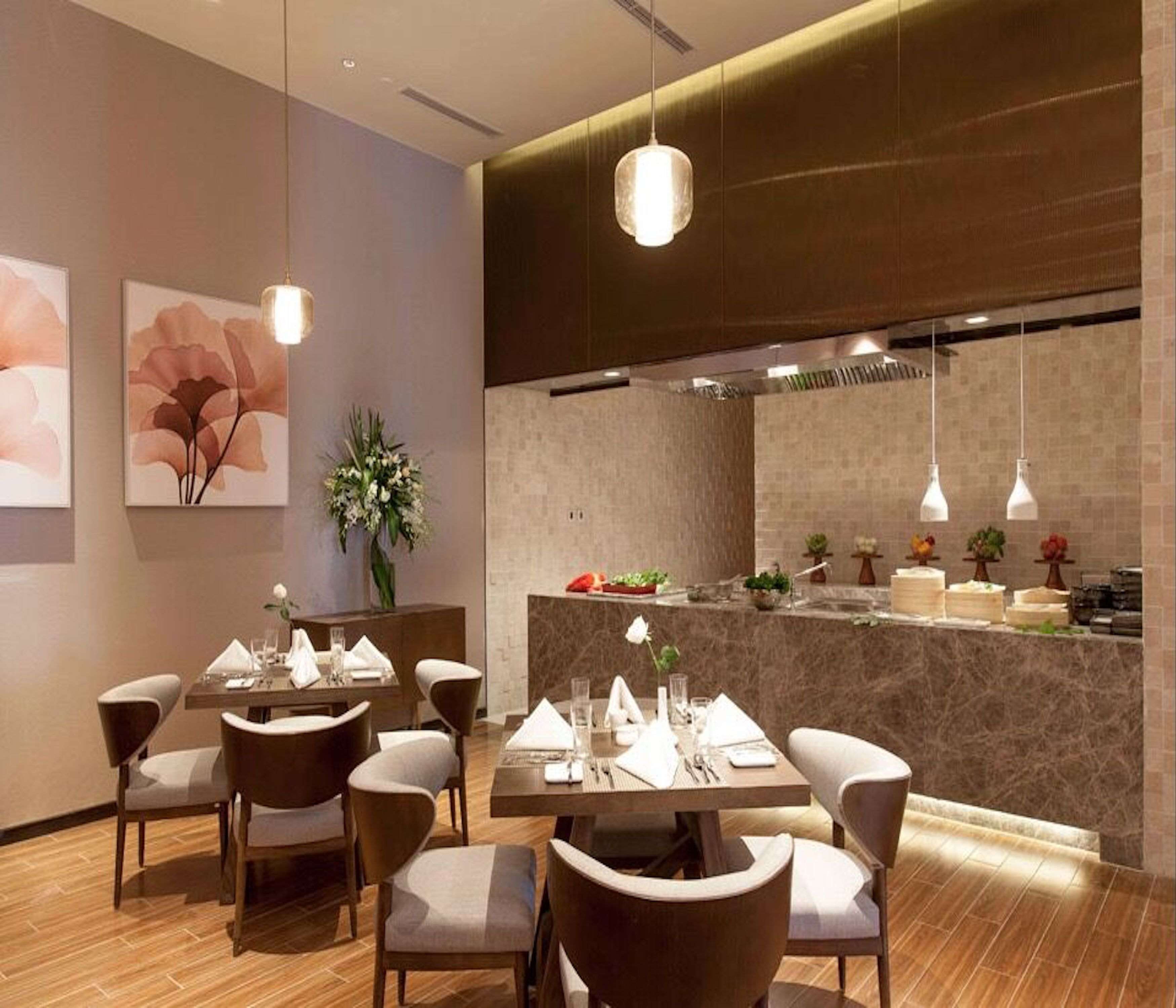 Un área de comedor moderna con mesas y sillas de madera, una encimera de mármol e iluminación colgante.
