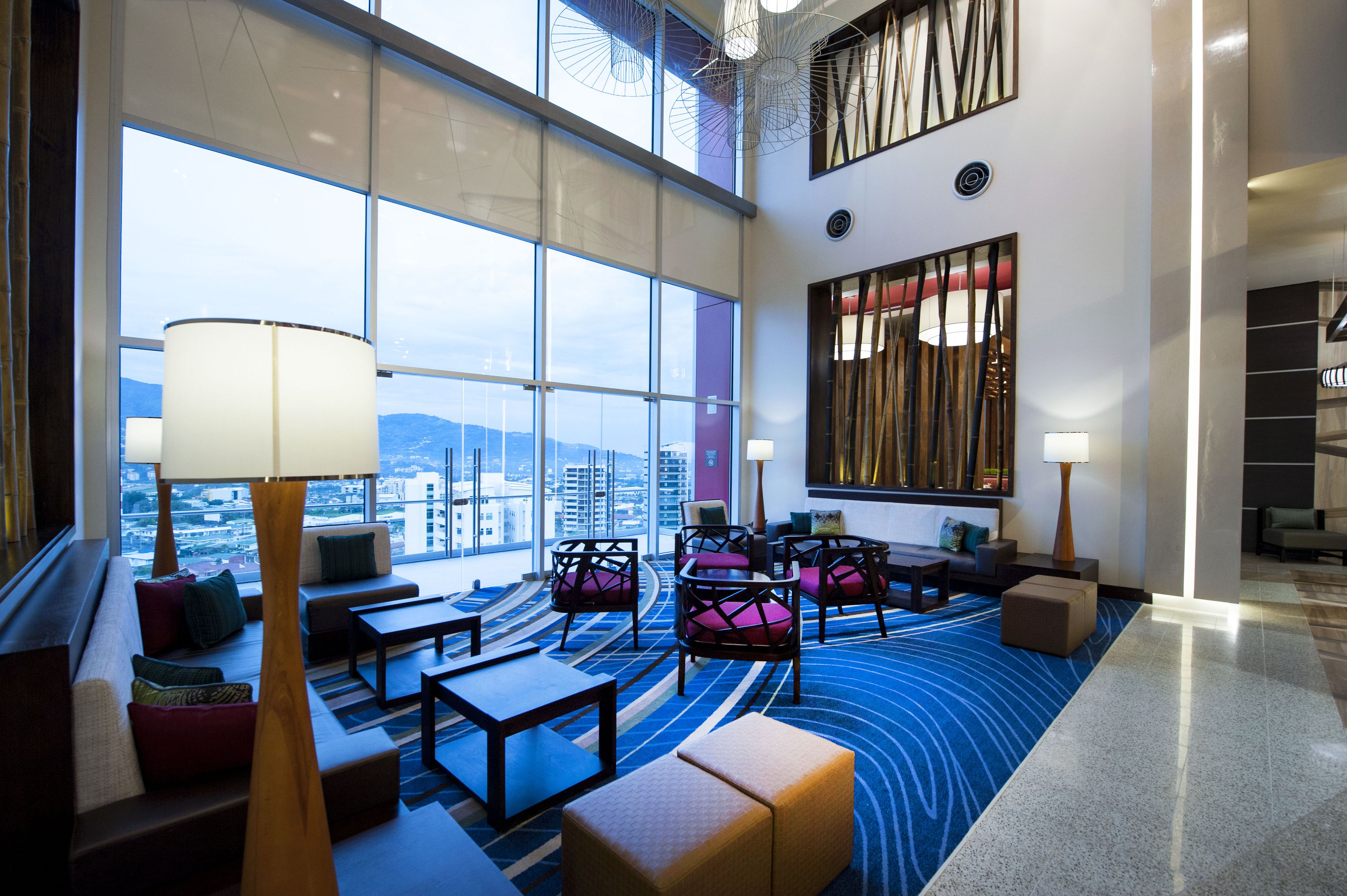 A modern hotel lobby with large windows, seating areas, and a view of the cityscape.