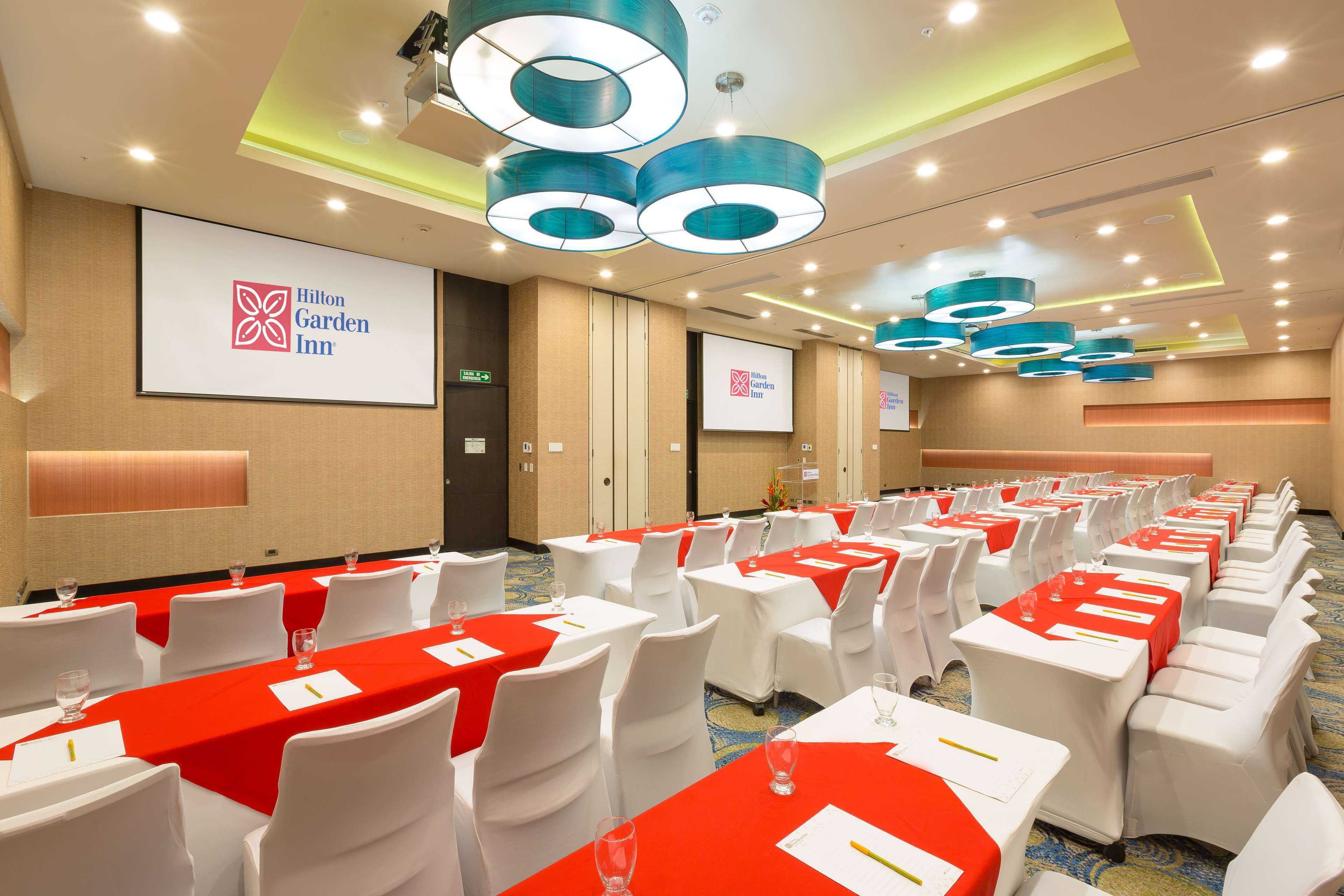 A conference room with rows of tables, white chairs, and red tablecloths at Hilton Garden Inn.