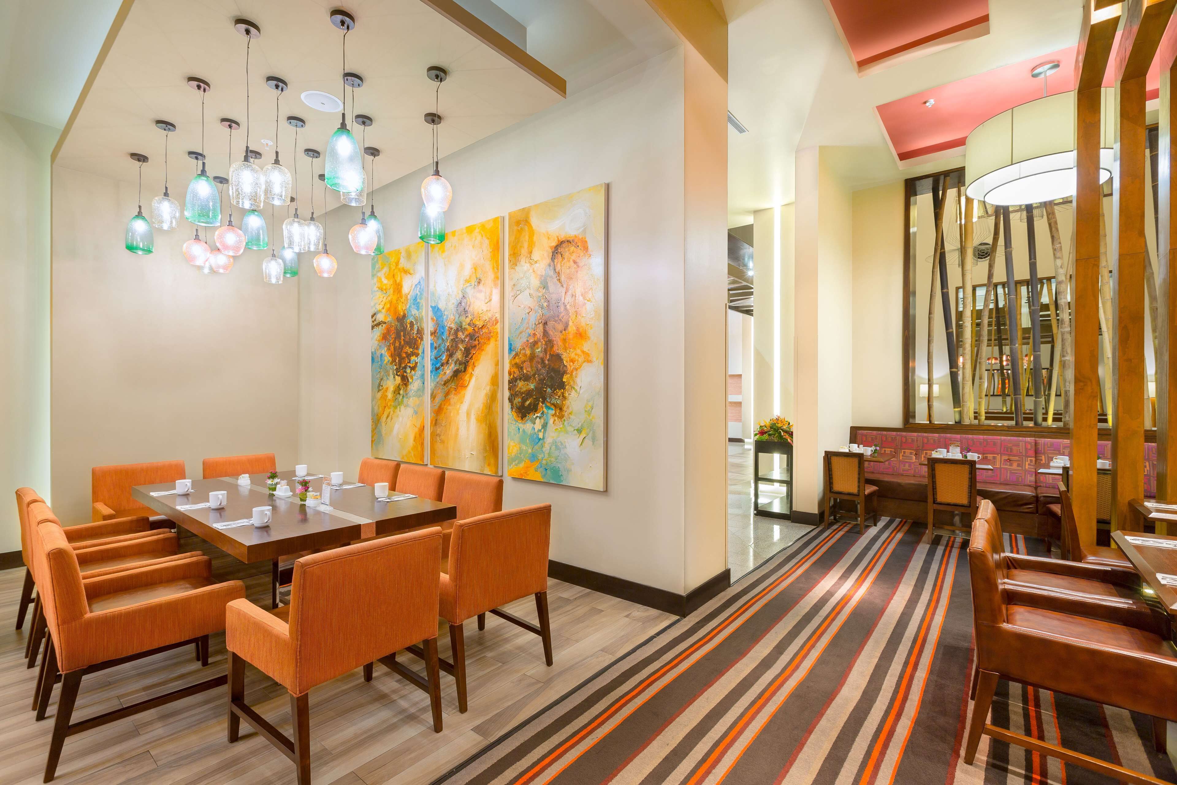 Un comedor con una larga mesa y sillas naranjas, un cuadro abstracto grande en la pared y una alfombra a rayas.