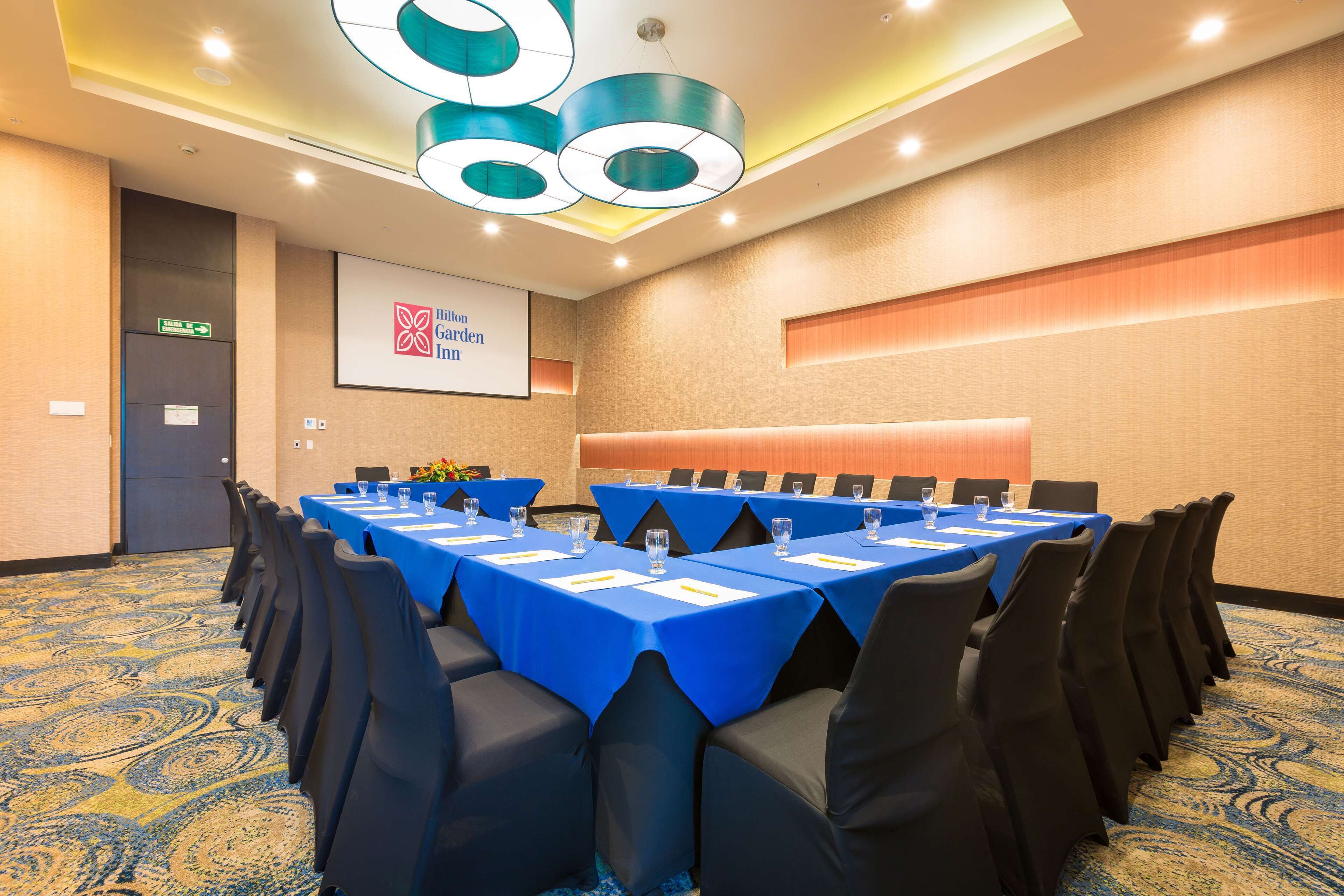 A conference room with tables and chairs, a projector screen, and a sign indicating the Hilton Garden Inn.