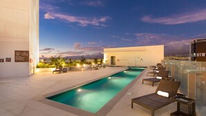Zona de piscina con sillones de descanso y vistas a la ciudad al atardecer.