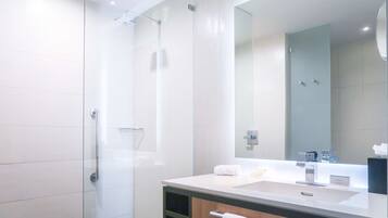 A modern bathroom with a glass shower enclosure, a large mirror, and a white sink.