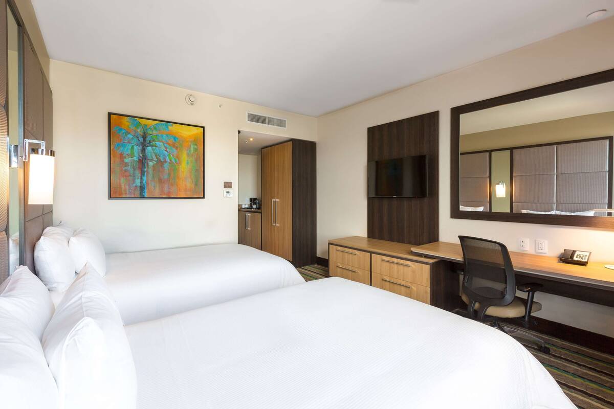 Een hotelkamer met twee bedden, een bureau, een stoel, een televisie en een schilderij aan de muur.