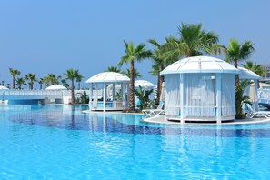 Una piscina con agua azul cristalina, rodeada de palmeras y cabañas blancas.