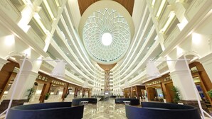 A spacious lobby with a central atrium, multiple floors, and a modern chandelier. - Sueno Hotels Deluxe Belek - All Inclusive (Serik)