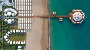 An aerial view of a beach resort with a pier extending into the sea, featuring sun loungers and umbrellas. - Sueno Hotels Deluxe Belek - All Inclusive (Serik)