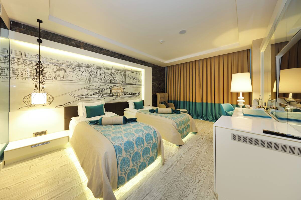 Ein Hotelzimmer mit zwei Betten, einem großen Wandbild, einem Schreibtisch und einem Spiegel.