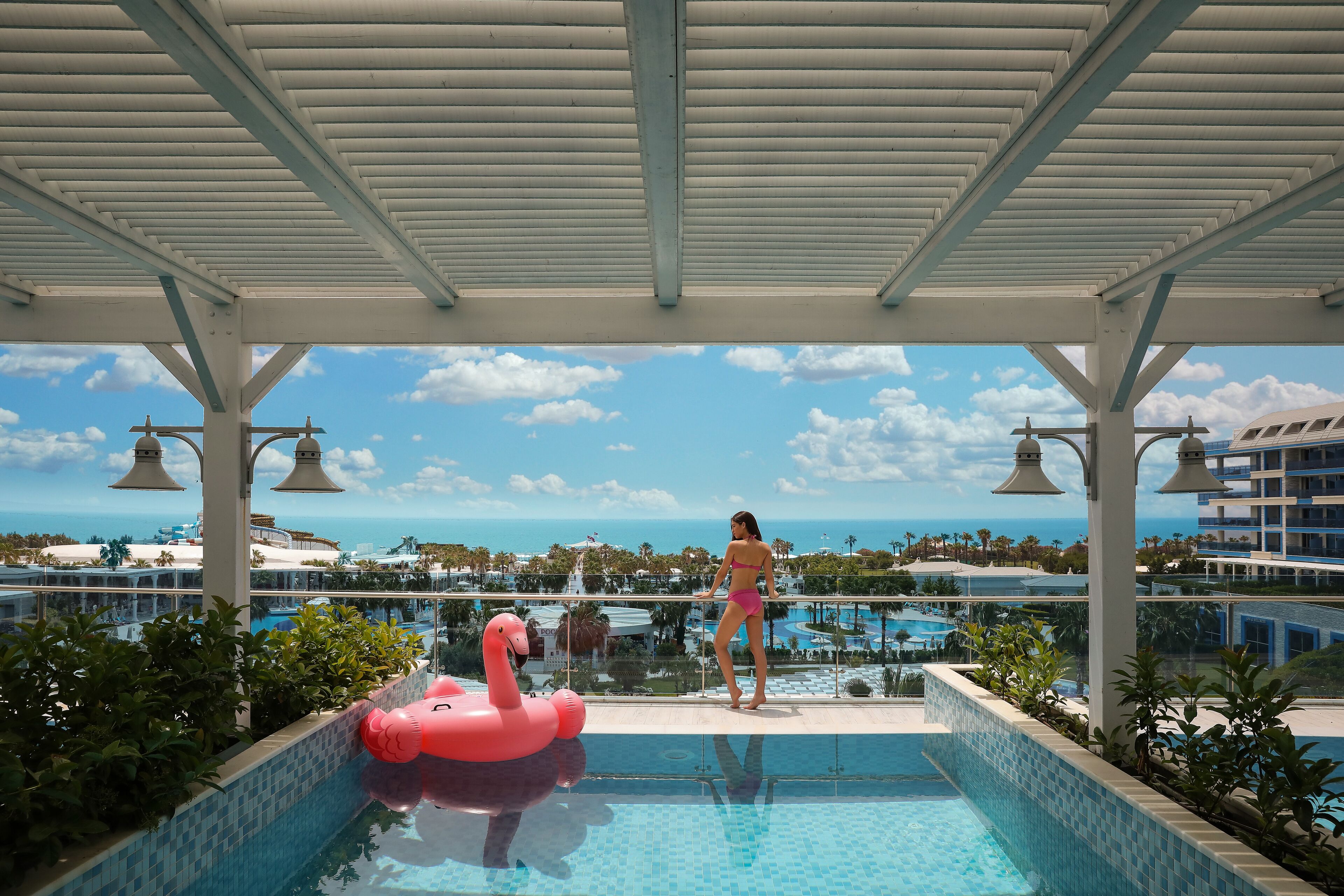 A pool area with a view of the ocean, a pink flamingo float, and a covered seating area.