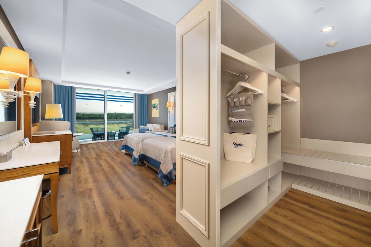 Ein Hotelzimmer mit einem großen Bett, einem Schreibtisch, einem Stuhl, einem Kleiderschrank und Blick ins Freie.