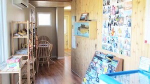 A room with wooden walls, a wooden floor, a chair, a small table with a box, and a bulletin board with photos.