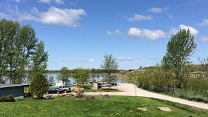 A lakeside property with a grassy lawn, a dirt path, and a small building.