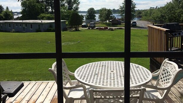 A patio with a round table and chairs, overlooking a grassy yard and a lake.